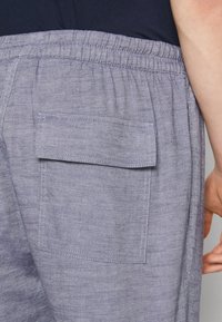 Šedé lněné kalhoty s elastickým pasem a jednou zadní kapsou. Látka má texturovaný, tkany vzhled.