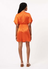 Kurzes, orangenes Satin-Kleid mit tailliertem Bund, lockeren Ärmeln und leicht ausgestelltem Saum. Glatte Textur und einfaches, elegantes Design.