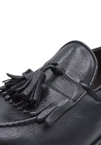 Czarne skórzane półbuty z teksturowanym wykończeniem, okrągłym noskiem i dekoracyjnymi frędzlami na wierzchu, z przeszyciami wzdłuż krawędzi.