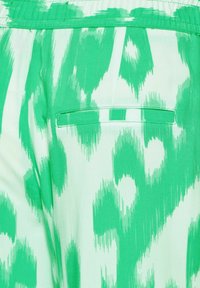 Grönmönstrad tyg som erbjuder en blandning av ljusa och mörka gröna nyanser med en subtil textur. Inkluderar ett bakfack med en horisontell klaff.