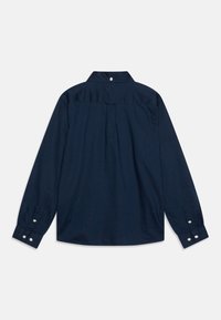 Granatowa koszula z długim rękawem, z kołnierzykiem zapinanym na guziki, pojedynczym fałdą z tyłu oraz mankietami zapinanymi na białe guziki. Gładka faktura.