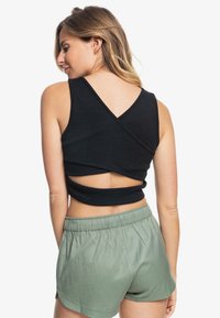 Top negro sin mangas con tejido texturizado, que presenta un diseño de espalda cruzada. Combinado con shorts verdes claros de cintura elástica.