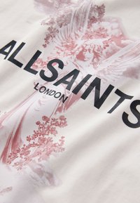 Illustrazione di angelo con ali e dettagli floreali dietro testo nero in grassetto "ALLSAINTS LONDON" su sfondo di tessuto chiaro.