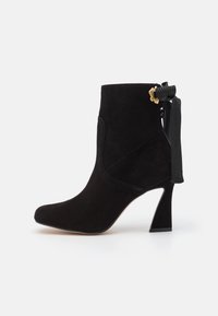 Musta mokkanahka nilkkaboots, jossa on korkea kaareva korko, sivuvetoketju ja koristeellinen musta nauha kultaisella yksityiskohdalla takana.