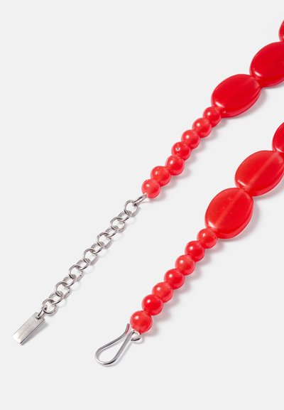 Κόσμημα λαιμού με κόκκινες χάντρες, που περιλαμβάνει μια ποικιλία από στρογγυλές και ωοειδείς χάντρες. Διαθέτει μεταλλική αλυσίδα με κλείσιμο από καβίλια για ασφαλές κλείσιμο. Λείο υφές, γυαλιστερή επιφάνεια.