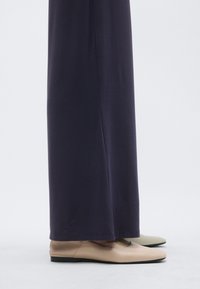 Bezas dzīvokļveida kurpes ar gludu, matētu virsmu, kombinētas ar vaļīgu, tumši violets audumu, radot vienkāršu, mūsdienīgu apģērba tēlu.