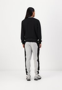 Hanorac negru cu guler rotund, mâneci lungi și detalii cu logo. Pantaloni de trening gri cu panouri negre pe laterale; ambele oferă o croială lejeră.
