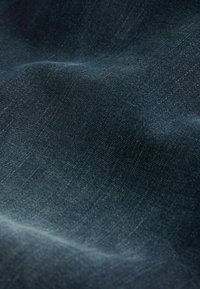 Dunkelblauer, strukturierter Stoff mit dezenter diagonaler Webstruktur, zeigt weiche Falten und sanfte Schatten.