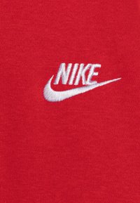 Material din bumbac roșu, cu un logo alb brodat "NIKE" și un swoosh. Designul este simplu și modern.