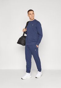 Navyblauwe sweatshirt en joggers, van een katoenmix, met ribgebreide boorden, een bijpassend logo op de borst en op de broek, gecombineerd met een zwarte sporttas en witte sneakers.