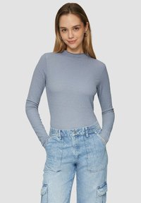 Hellblaues Langarmoberteil aus strukturiertem Stoff mit hohem Kragen, kombiniert mit hochgeschnittenen hellblauen Cargo-Hosen aus Denim mit Taschen.