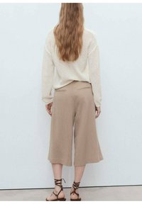 Beige wide-leg culottes with a smooth texture, featuring back pockets, paired with a cream loose-fitting sweater and brown strappy sandals.