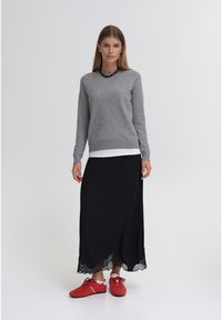 Sivi pulover z dolgimi rokavi čez belo majico, kombiniran s črno dolgo krilo z čipkasto obrobo in rdečimi športnimi čevlji. Preprost, večplasten slog.