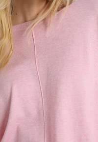 Różowy sweter wełniany o miękkiej teksturze, szerokim dekolcie i widocznych szwach biegnących w pionie. Wygodny i luźny krój.