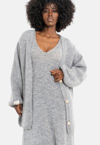 Szary sweter na drutach z dużymi rękawami, z drewnianymi guzikami i teksturowanym wykończeniem, noszony na szarą sukienkę o dopasowanym kolorze.