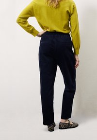 Pantalon en velours côtelé bleu marine avec une coupe décontractée, doté de poches arrière. Associé à un pull vert vif et des chaussures à imprimé léopard.