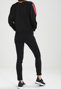 Sudadera negra de manga larga con detalles en rojo, combinada con unos jeans negros ajustados y zapatillas negras con detalles en azul claro.