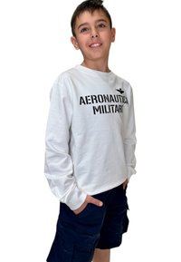 Camicia bianca a maniche lunghe con la scritta "AERONAUTICA MILITARE" stampata in nero, abbinata a pantaloni cargo blu navy con tasche laterali.