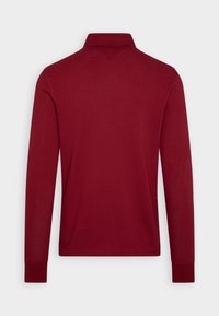 Poloko s dlouhými rukávy v tmavě burgundské barvě, s klasickým límcem, žebrovanými manžetami a hladkou, bavlněnou texturou. Žádné vzory nejsou viditelné.