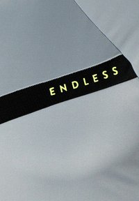 Grijze stoffen top met een zwarte band met de tekst "ENDLESS" in het geel. Soepele textuur met een gestroomlijnd ontwerp.