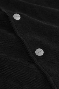 Black corduroy fabric with vertical ribbing, featuring silver metal buttons stamped with "DON'T WASTE CULTURE." Texture appears soft.