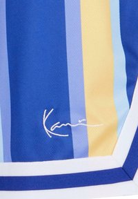 Kombinasjonsstoff i bomull med vertikale striper i blå, lyseblå, gul og krem. Inkluderer hvit pynt og en brodert signaturdetalj.