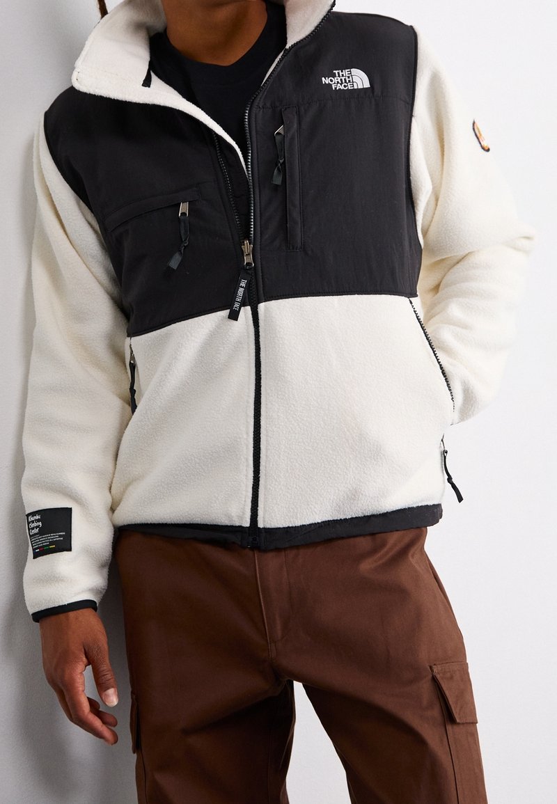 Fleecejacke mit schwarzen und cremefarbenen Einsätzen, durchgehendem Reißverschluss, mehreren Taschen und kontrastierenden Bündchen. Mit Markenlogo auf Brust und Ärmel.