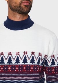 Pull blanc avec un col côtelé bleu marine et un motif festif. Il présente des arbres et des flocons de neige en rouge et bleu marine. Texture tricotée, design ajusté.