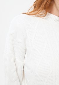 Biały sweter robiony na drutach z prążkowaną fakturą i wzorem w diamenty. Posiada wysoki kołnierz i lekko oversize'owy krój. Miękka, przytulna tkanina.