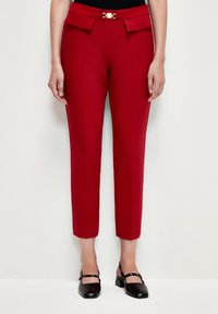 Pantalones rojos ajustados con cintura alta, parte delantera plana con dos detalles de lazo y un broche dorado. Acabados con piernas recortadas y acampanadas.