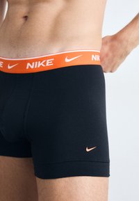 Fekete pamut boxer alsónadrág narancssárga Nike logóval a derékrészen és a lábszáron. Szoros fazonú és sima textúrájú.