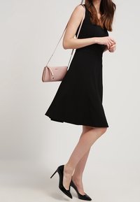 Schwarzes A-Linien-Kleid mit tailliertem Oberteil und ausgestelltem Rock, kombiniert mit einer rosa Umhängetasche und schwarzen High Heels. Glatte Stofftextur.