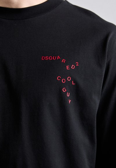Must musta särk mustast puuvillast, millel on punane kiri "DSQUARED2 COOL GUY", mis on paigutatud dünaamilises vormis rinnaosa.