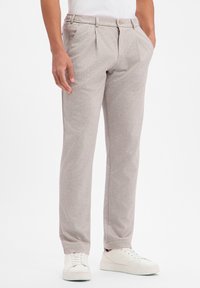 Jasnoszare spodnie z teksturowanej tkaniny, z przodem z zakładkami, elastycznym paskiem i subtelnymi kieszeniami, zestawione z białymi trampkami.