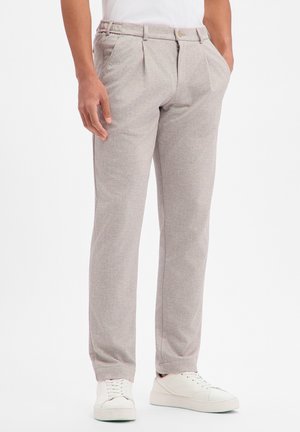 Pantaloni grigio chiaro con tessuto strutturato, design anteriore plissettato, vita elasticizzata e tasche discrete, abbinati a scarpe da ginnastica bianche.