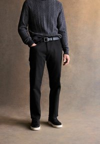 Fekete szabott nadrág, amelyhez egy textúrált sötétszürke pulóver tartozik, herringbone mintázattal; fekete nubuk tornacipővel és fekete övvel viselve.