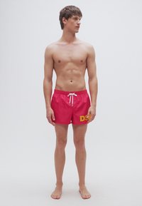 Κόκκινα μαγιό σορτς με λευκό κορδόνι στη μέση και έντονο κίτρινο κείμενο "DSI" στο αριστερό πόδι. Το υλικό φαίνεται ελαφρύ και λείο, κατάλληλο για νερό.