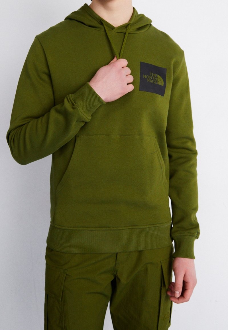 Bluza z kapturem w oliwkowej zieleni, wykonana z miękkiego materiału, z kieszenią z przodu i czarną naszywką z logo na piersi, z prążkowanymi ściągaczami przy mankietach i u dołu.