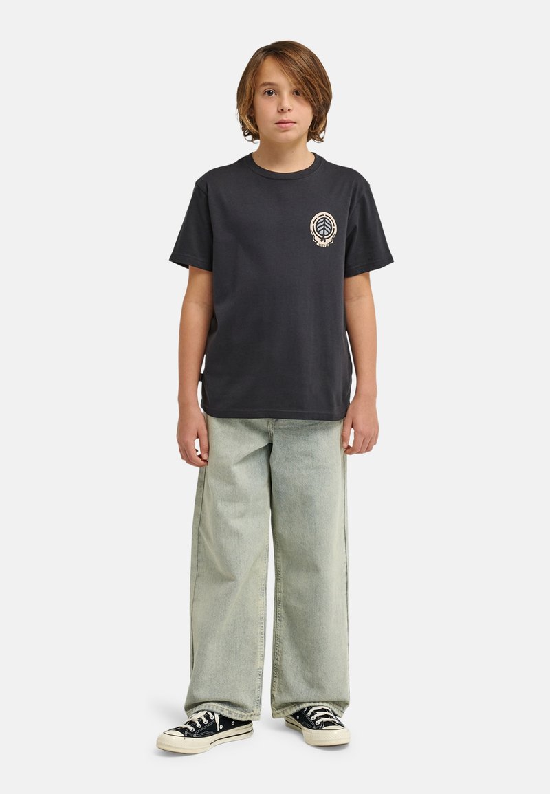 Camiseta negra de algodón con un logo de hoja en el pecho, combinada con jeans azul claro de corte holgado y zapatillas negras de caña baja.