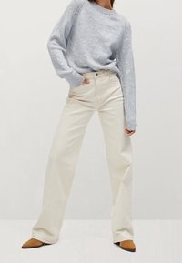 Un pull en tricot bleu clair avec un col en côtes, associé à un pantalon en jeans crème à jambes larges. Des chaussures pointues marron complètent la tenue.