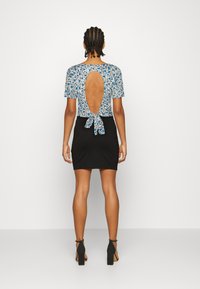 Blusa floral com estampado azul e branco, apresenta um cost nas costas com um detalhe em laço. Combinada com uma saia preta justa e saltos altos.