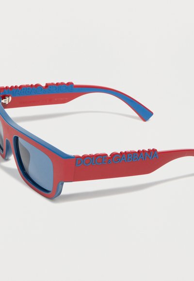 Ορθογώνια γυαλιά ηλίου σε κόκκινο και μπλε χρώμα με φακούς βαμμένους μπλε και ανάγλυφο μπλε λογότυπο "DOLCE & GABBANA" στο κόκκινο πλευρικό σκέλος.