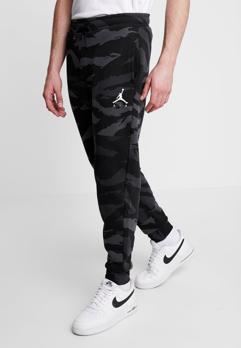 Černé a šedé maskáčové tepláky s elastickým pasem a manžetami, na levém stehně se nachází bílé logo Jordan. Doplněno bílými teniskami Nike.