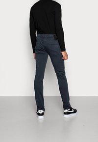 Grå slim-fit byxor med flera fickor, en svart etikett på midjan, bärs med svart och vita sneakers. Slät tygkvalitet.