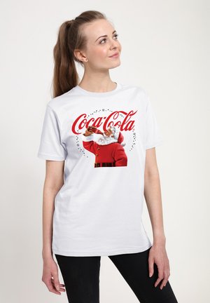 Biała bawełniana koszulka z grafiką Świętego Mikołaja w czerwonym garniturze pijącego z butelki Coca-Coli, z czerwonymi napisami i dekoracyjnymi akcentami.