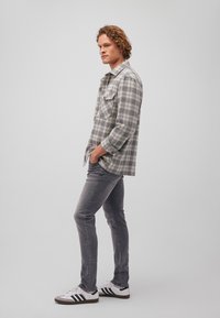 Grau-weiße karierte Button-up-Hemd mit zwei Brusttaschen, kombiniert mit grauen Jeans und weißen Sneakern mit schwarzen Streifen.