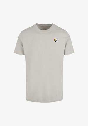 T-shirt en coton gris clair avec des manches courtes et un col rond, arborant un petit emblème en forme de cœur arc-en-ciel sur la partie gauche de la poitrine.