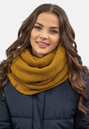 Écharpe infini tricotée jaune moutarde avec un motif texturé, portée sur une veste marine. Présente une petite étiquette de marque marron.