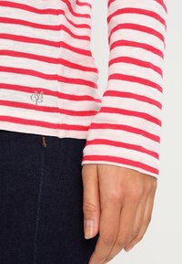 Maglietta a maniche lunghe a righe rosse e bianche realizzata in tessuto morbido, con un logo sul fondo, abbinata a jeans scuri.