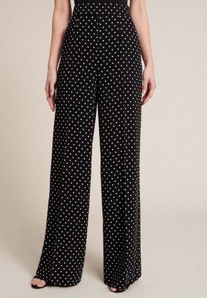 Sorte vidde bukser med hvide polkaprikker båret af en stående person, kombineret med sorte sandaler med åbne tæer.